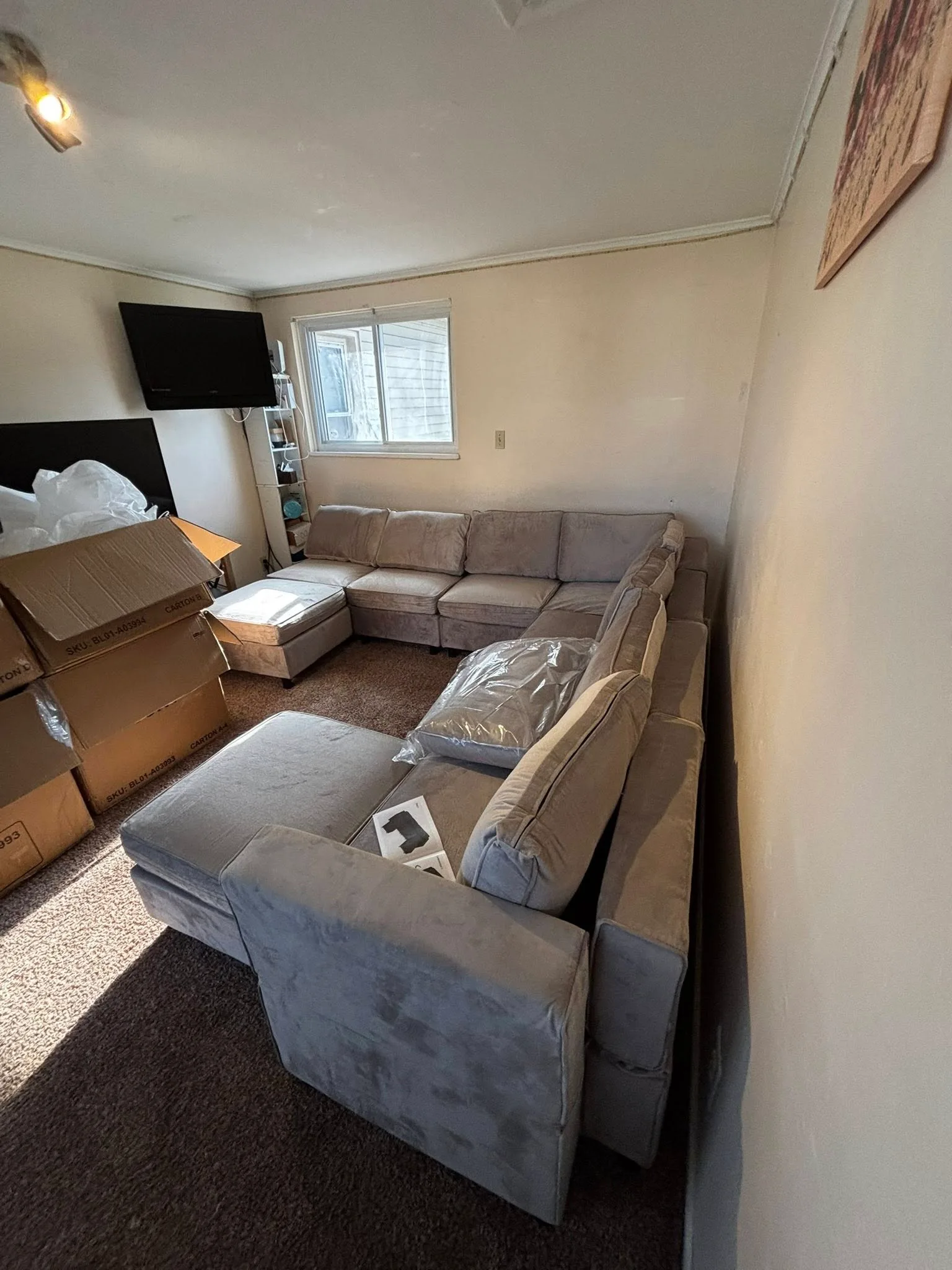The same room with the sectional fully assembled in grey, and the TV wall-mounted behind it.